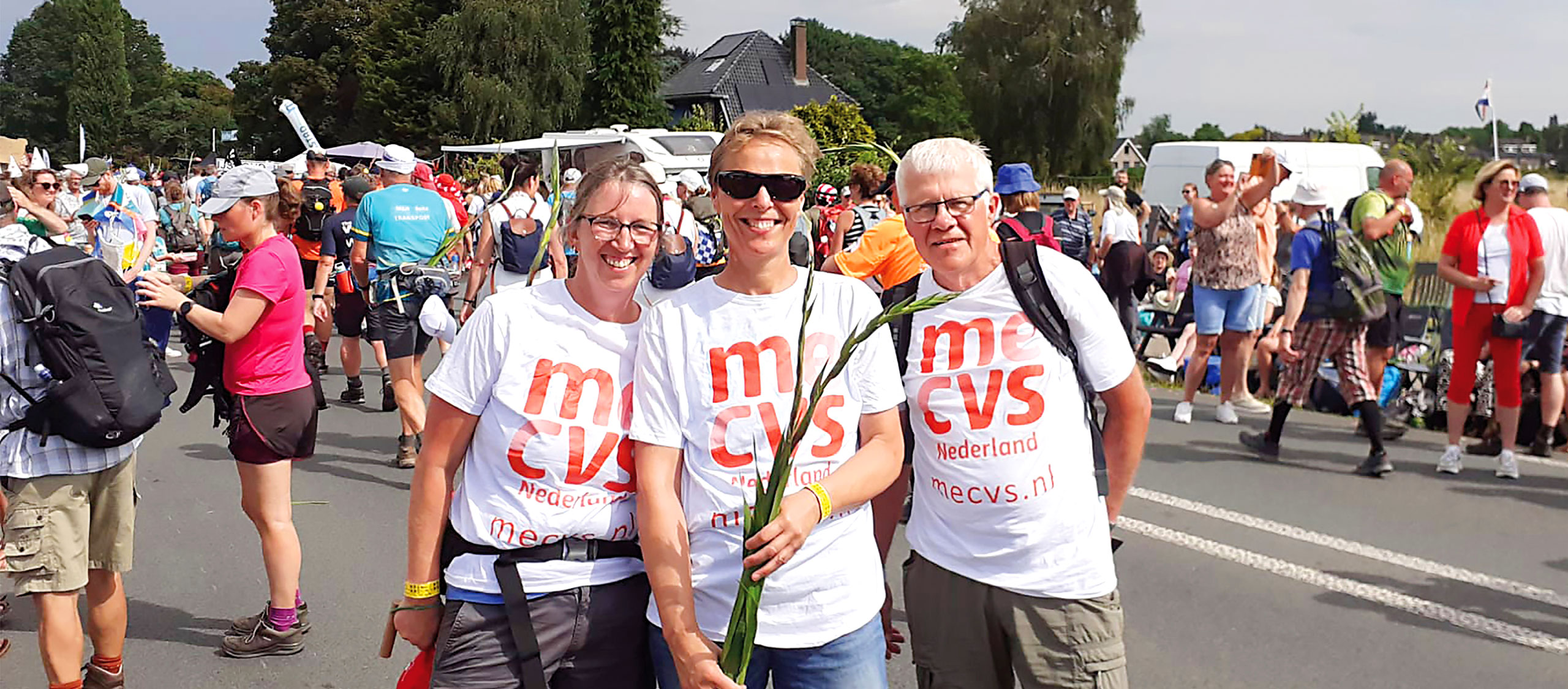 HSTotaal: banner met drie sponsorlopers in witte t-shirts met rode logo van MECVS Nederland tijdens Vierdaagse van Nijmegen