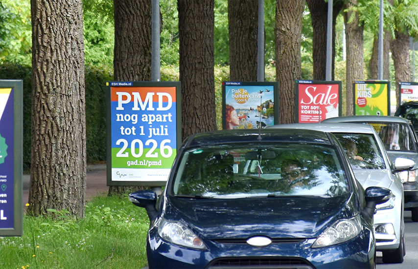 HSTotaal: auto’s rijden in Hilversum langs abri posters die tussen de bomen staan; de GAD-poster over afvalscheiding valt op