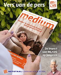 Een vrouw houdt het omslag van de september MEdium omhoog terwijl ze in de tuin bij een groene haag zit.